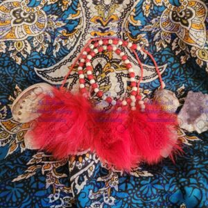 A handmade jewelry set featuring red and white beaded earrings with red fox fur accents and a matching beaded necklace. The set is arranged on a blue and gold paisley-patterned fabric background, alongside a small amethyst cluster and a shell.