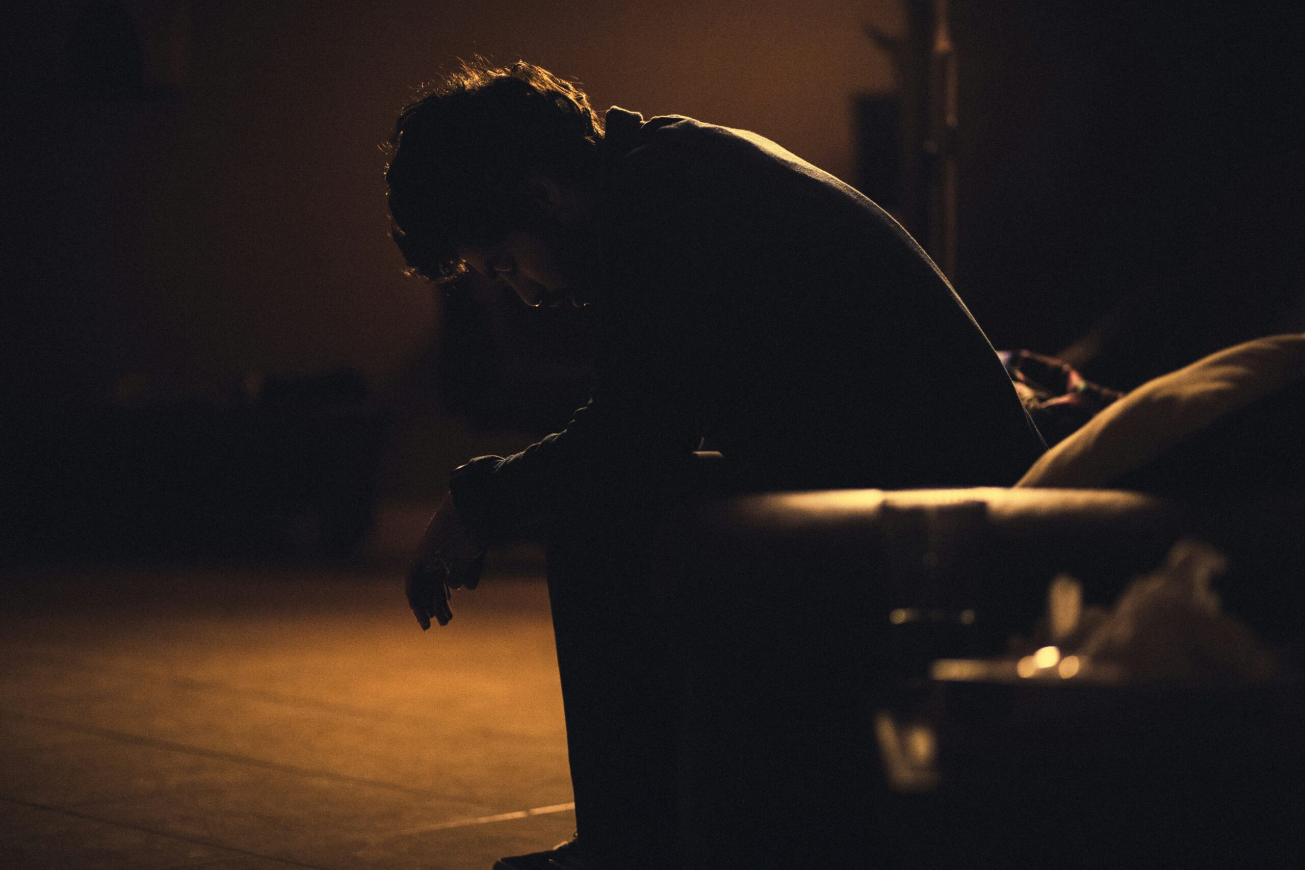 an image by gadiel lazcano on unsplash. Depicts a person sitting hunched over in the dark.