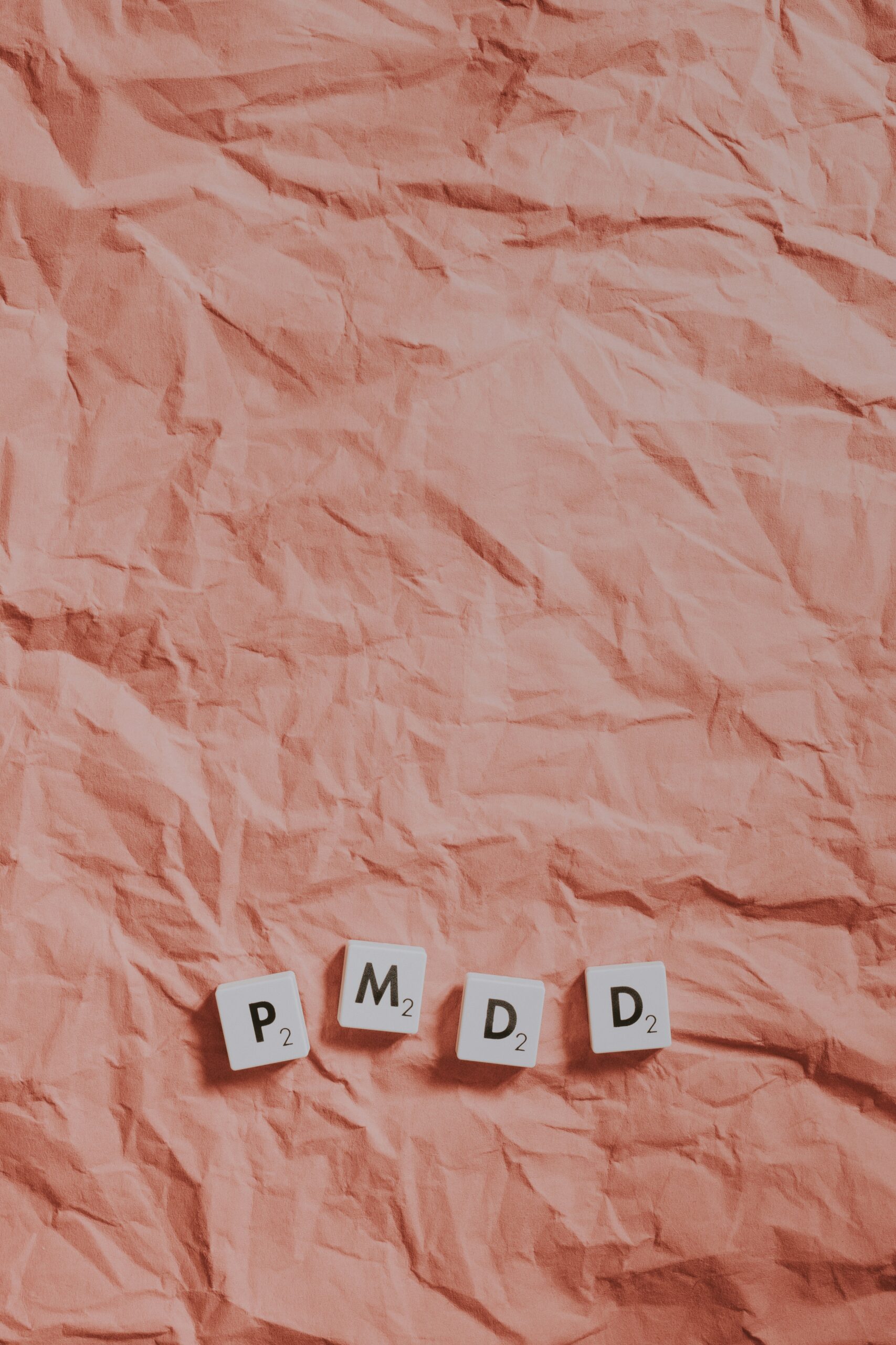 An image of Scrabble letters spelling out PMDD on a pink background. Photo by Pawel Czerwinski on Unsplash.